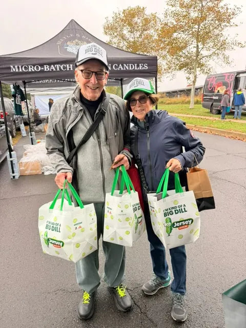 A couple carrying three Jersey Pickles totes at the farmers market