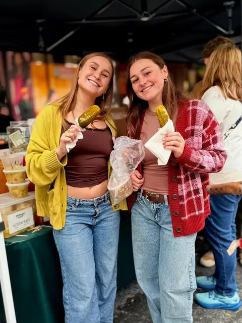 Two friends holding pickles on a stick at the Jersey Pickles stand